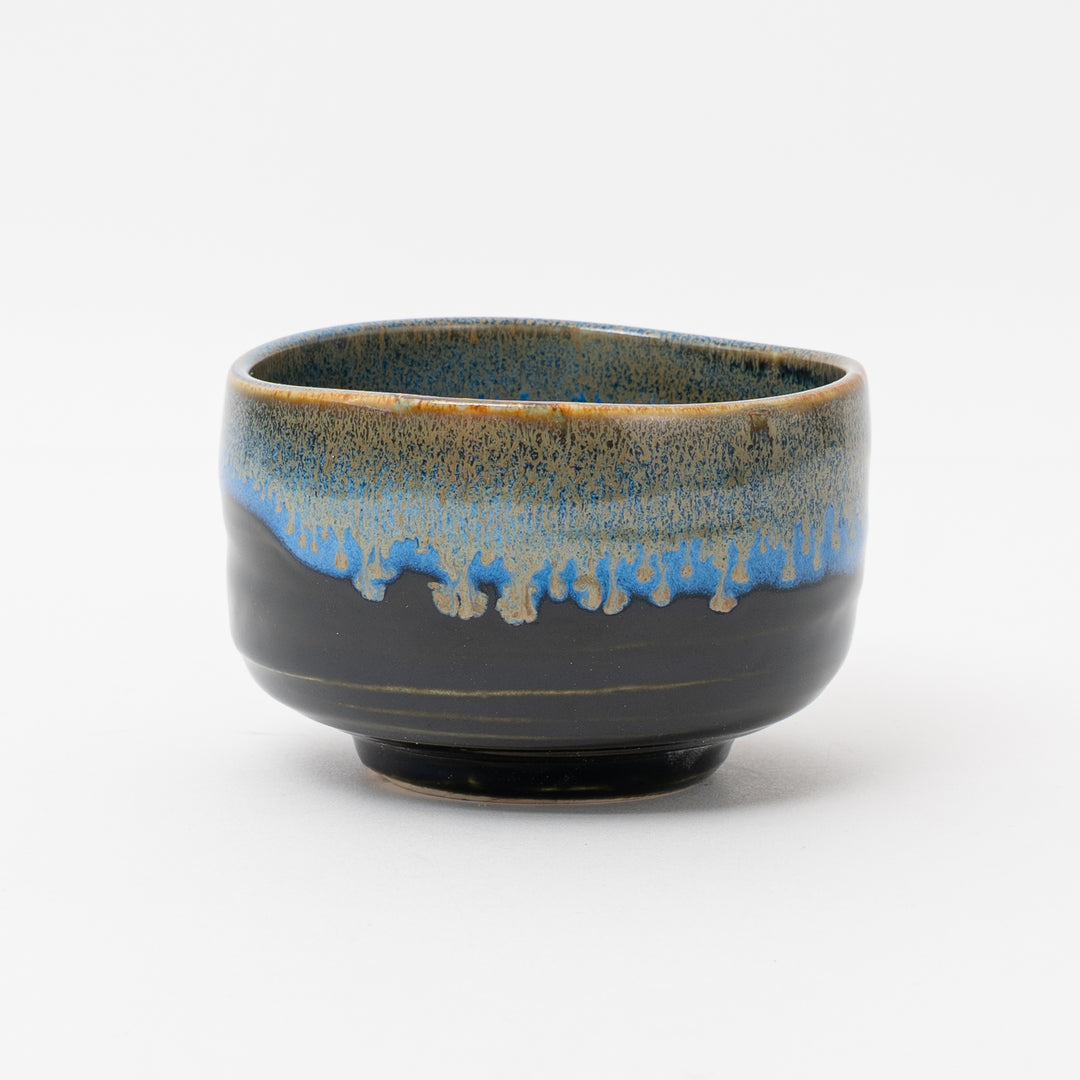A handmade Mino Ware matcha bowl from Japan with a glossy black glaze and a unique blue and brown drip glaze on the rim. The bowl has a smooth, polished finish.