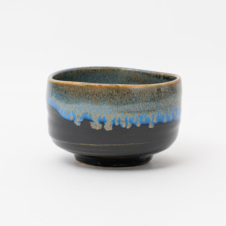 A handmade Mino Ware matcha bowl from Japan with a glossy black glaze and a unique blue and brown drip glaze on the rim. The bowl has a smooth, polished finish.
