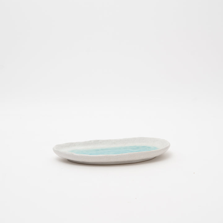 A side view of a small, handmade Japanese dish, highlighting its low profile and rustic, speckled texture, perfect for a side table.