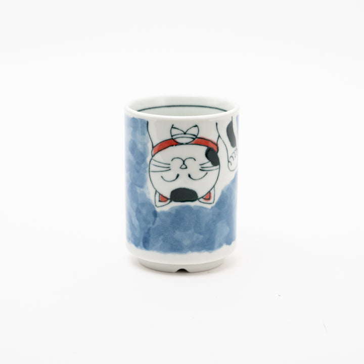 Side view of an authentic Japanese Maneki-Neko lucky cat porcelain cup with a hand-painted white cat, red collar, and blue background wash.