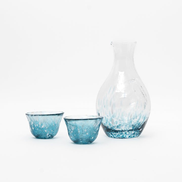 A handcrafted Toyo Sasaki Aqua Drizzle glass sake set with one carafe and two matching cups on a clean white background. The glassware features a unique turquoise and white speckled pattern, resembling gentle raindrops.