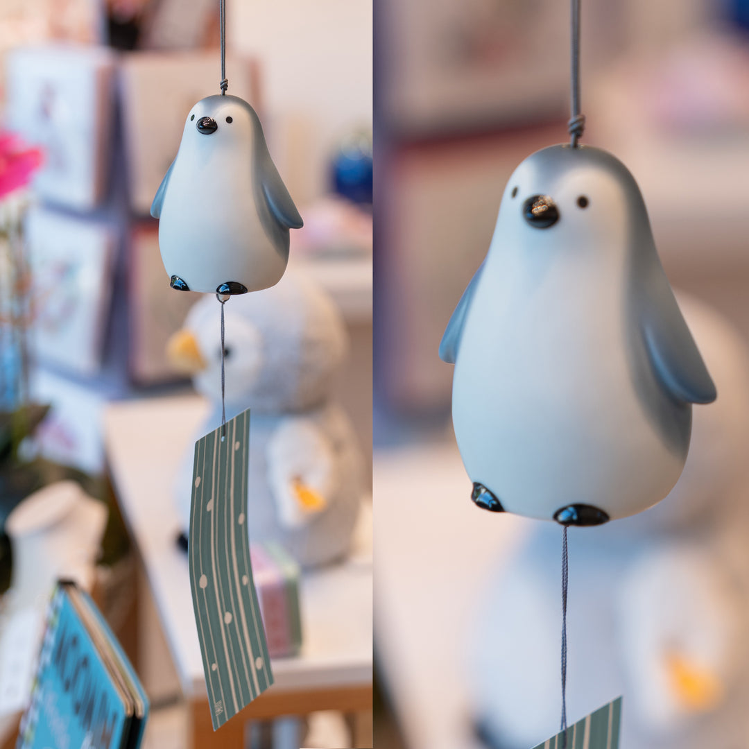 Yakushigama Japanese ceramic penguin wind chime on a white background, handmade with a blue striped paper tassel hanging from the bottom