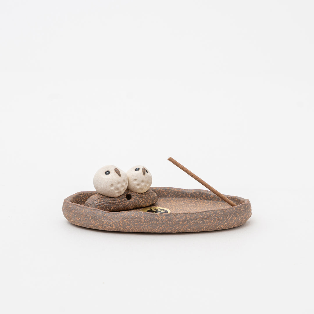 A handcrafted Shigaraki earthenware incense holder with a dish shape, featuring two white ceramic figures and a stick of incense.