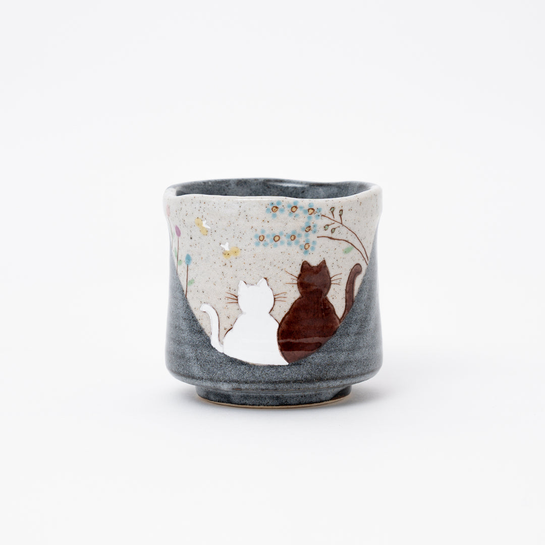 Hand-painted Kutani Ware Japanese ceramic tea cup (yunomi) with a serene design of two cats gazing at blue flowers on a speckled and dark gray glazed background.