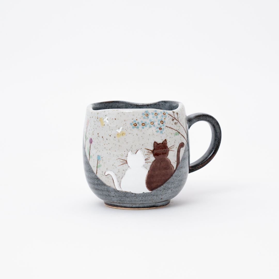 Hand-painted Kutani Ware Japanese ceramic coffee mug with a serene design of two cats gazing at blue flowers on a speckled and dark gray glazed background.