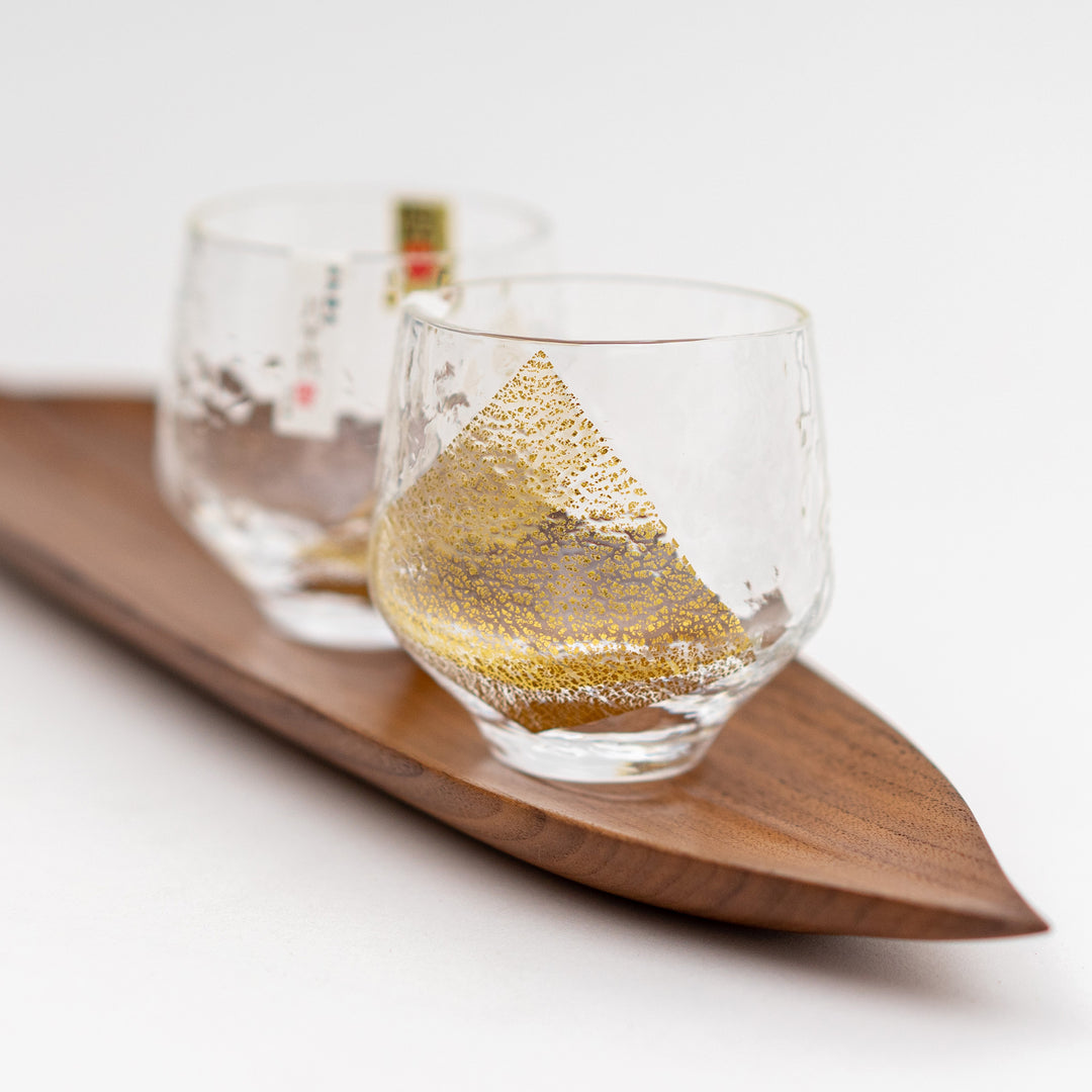 Two clear crystal sake cups with gold detailing, displayed on a wooden tray.