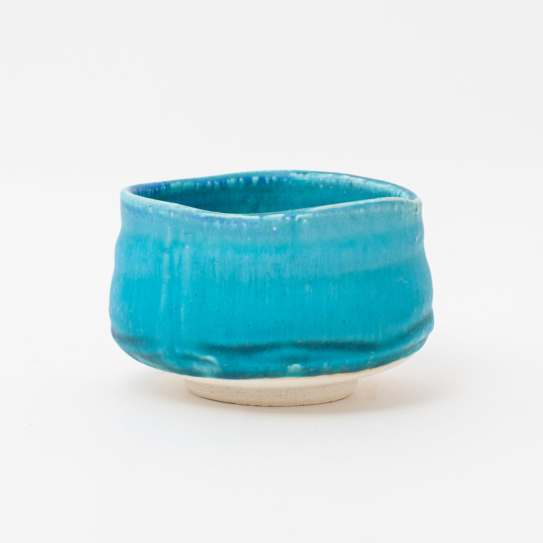 Handcrafted Mino Ware matcha bowl with a vibrant turquoise glaze, featuring a rustic texture and unique, irregular shape.

