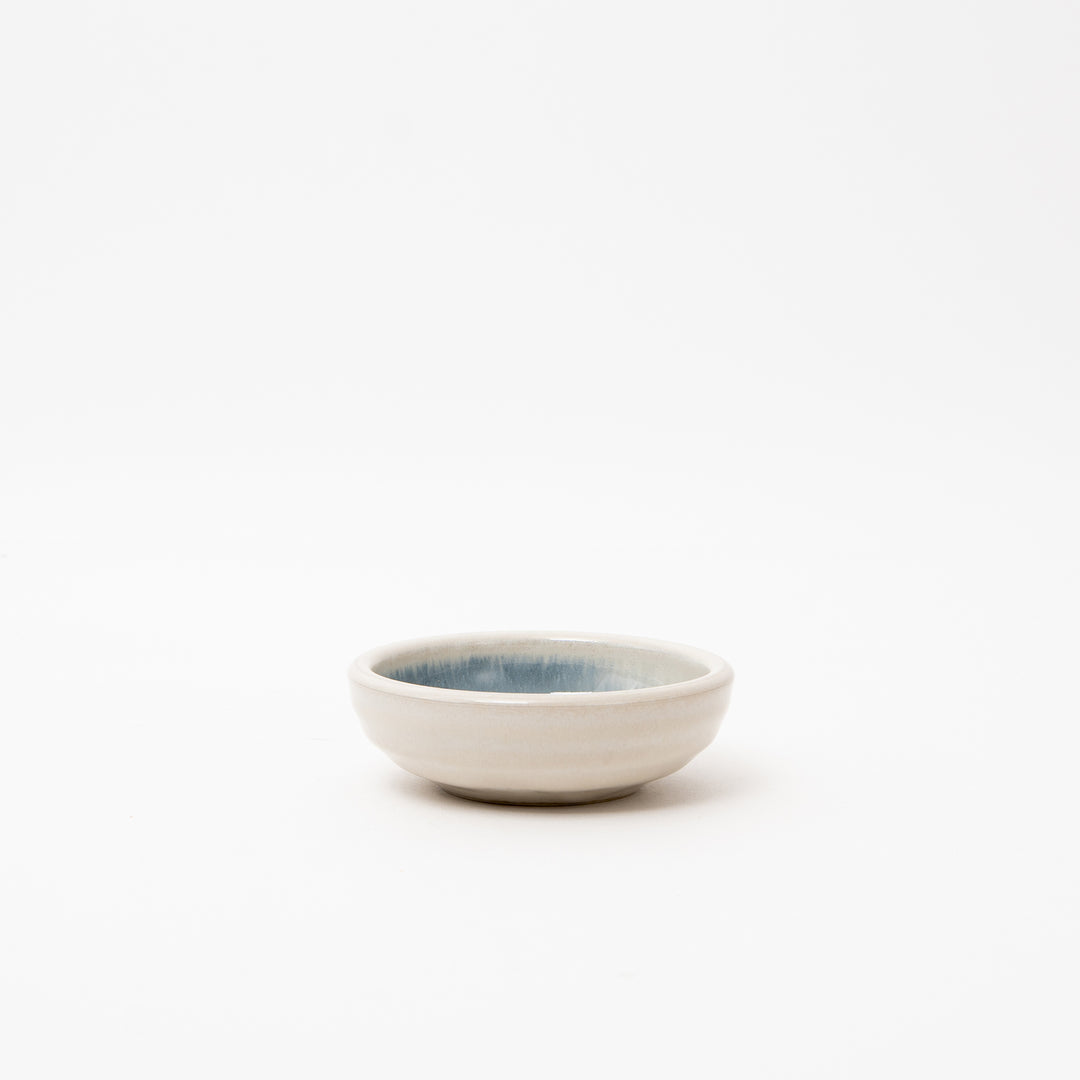 A side view of a small Japanese white ceramic dish with a smooth, blue brush design interior.