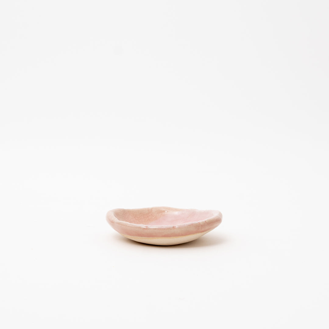 A side view of a small, irregularly shaped Japanese ceramic dish with a pink crackle glaze.