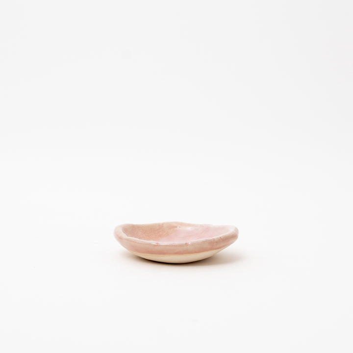 A side view of a small, irregularly shaped Japanese ceramic dish with a pink crackle glaze.