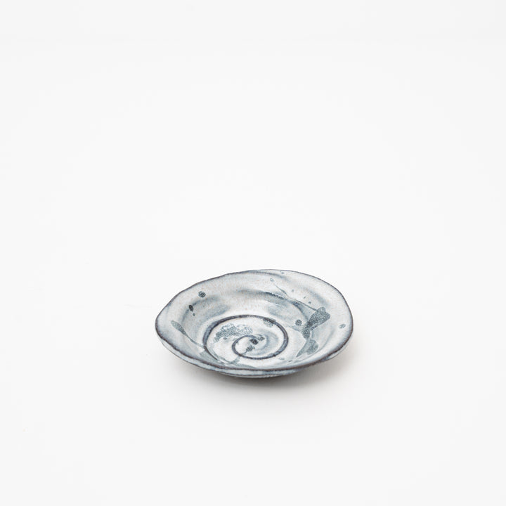 A side view of a small, irregularly shaped Japanese ceramic dish with a black spiral design on a light-colored base.