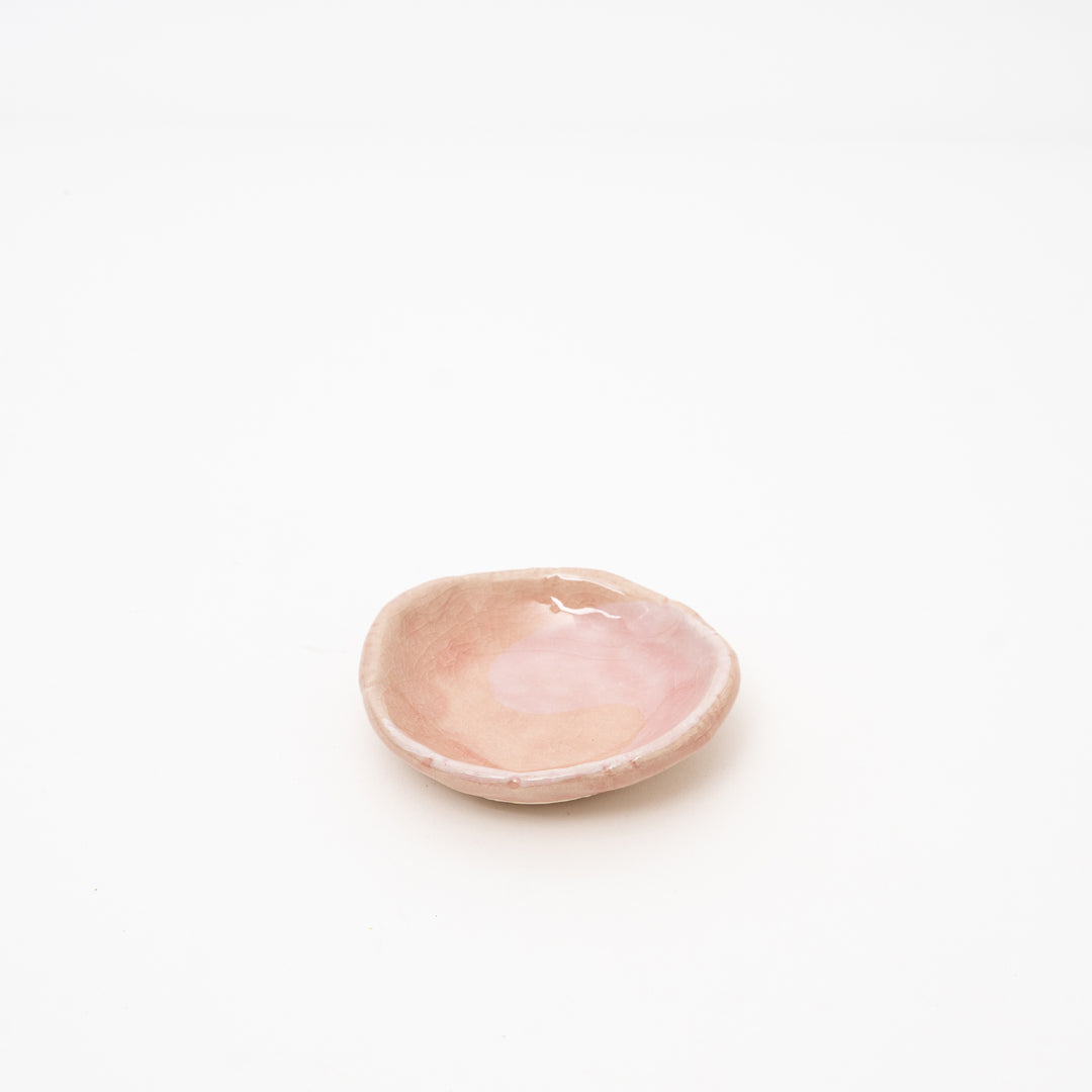 A top-down view of a small, irregularly shaped Japanese ceramic dish, showing the intricate pink crackle glaze pattern.