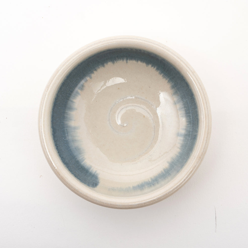 A top-down view of a small Japanese white ceramic dish, showing the unique blue brush design on the interior.