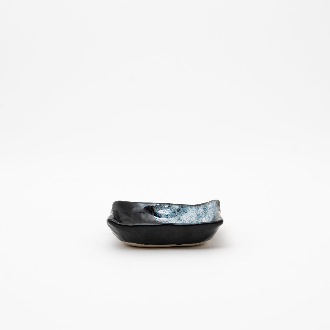 A side view of the square ceramic bowl, highlighting its low profile and organic, slightly wavy shape.