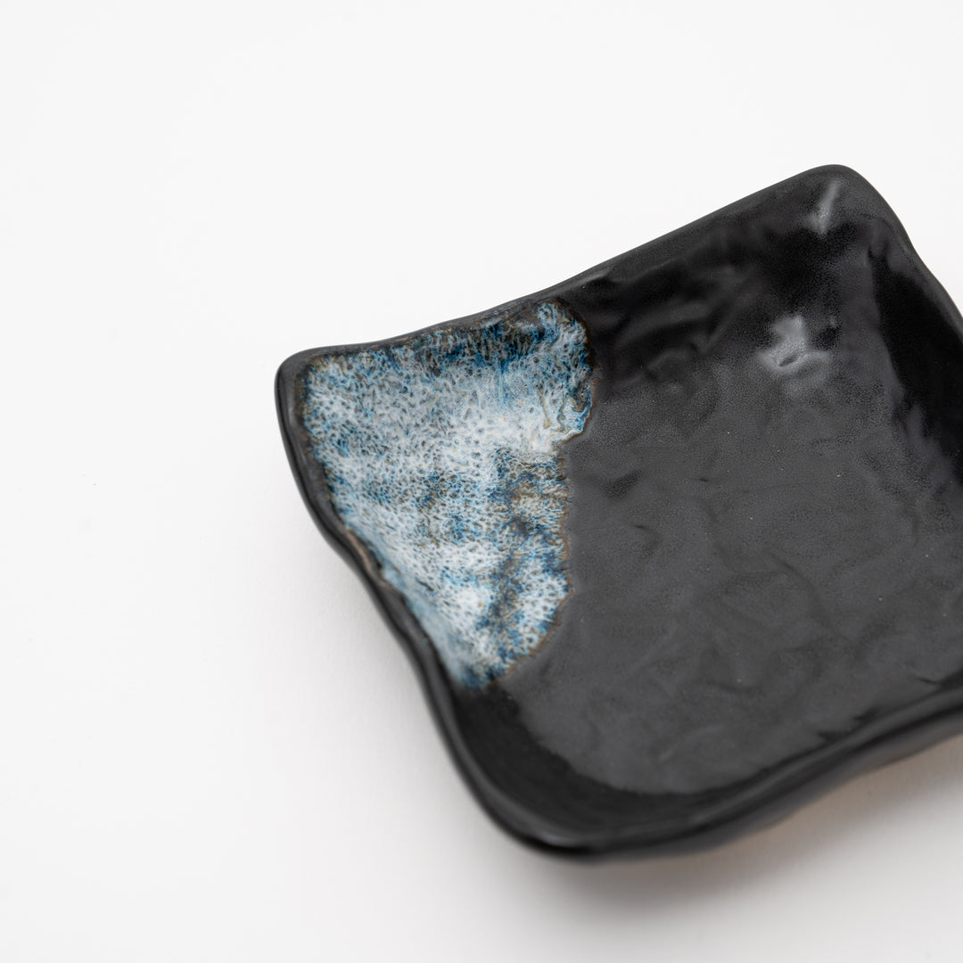 An overhead view of a handmade black square bowl with a distinct blue and white "Melted Snow" glaze detail on two corners.