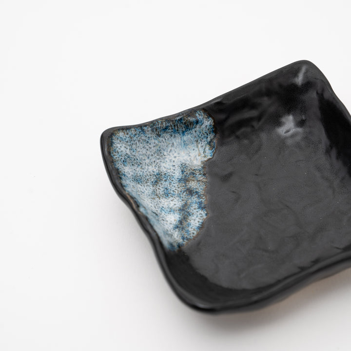 An overhead view of a handmade black square bowl with a distinct blue and white "Melted Snow" glaze detail on two corners.