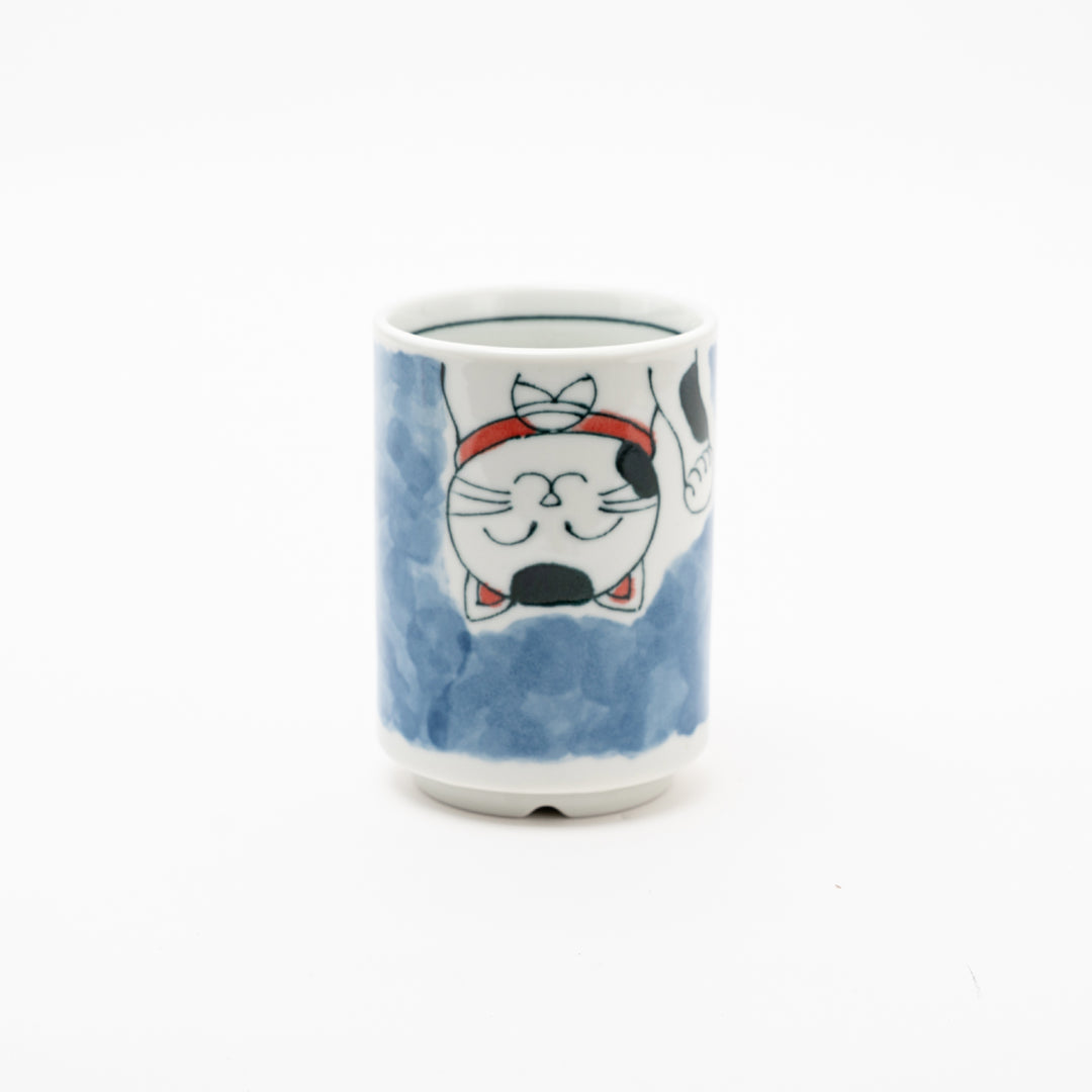 Side view of an authentic Japanese Maneki-Neko lucky cat porcelain cup with a hand-painted white cat, red collar, and blue background wash.