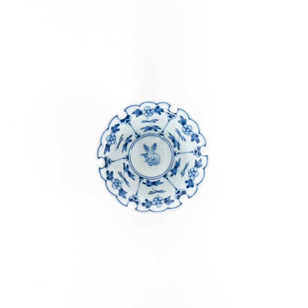 Top view of a Japanese Hasami ware mini bowl featuring a blue hand-painted rabbit crest and floral patterns with a scalloped snow ring rim.