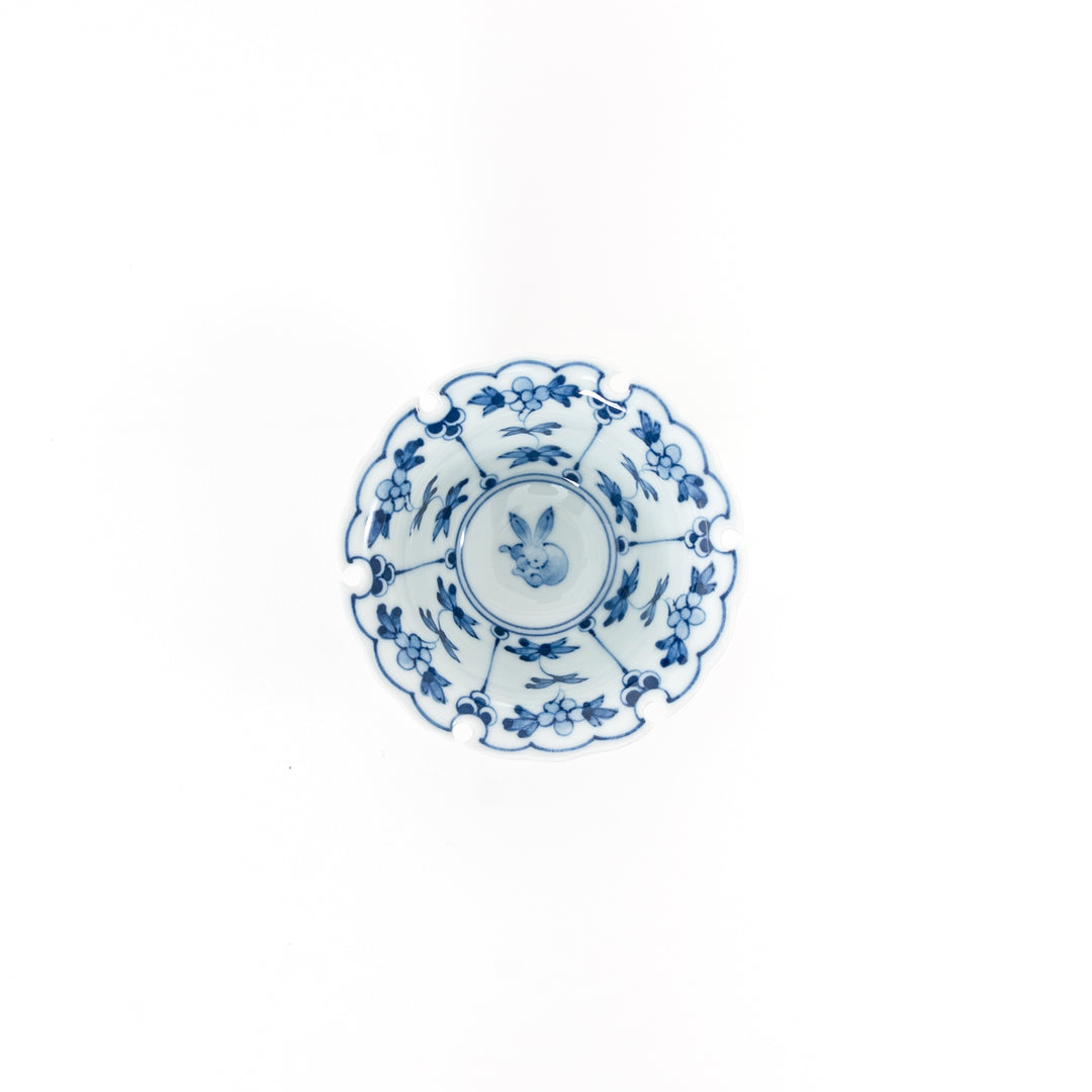 Top view of a Japanese Hasami ware mini bowl featuring a blue hand-painted rabbit crest and floral patterns with a scalloped snow ring rim.