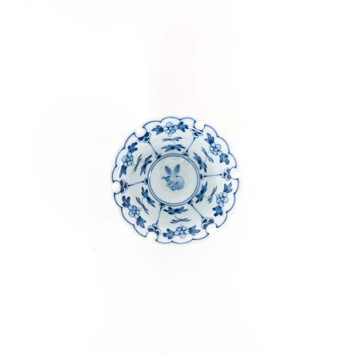 Top view of a Japanese Hasami ware mini bowl featuring a blue hand-painted rabbit crest and floral patterns with a scalloped snow ring rim.