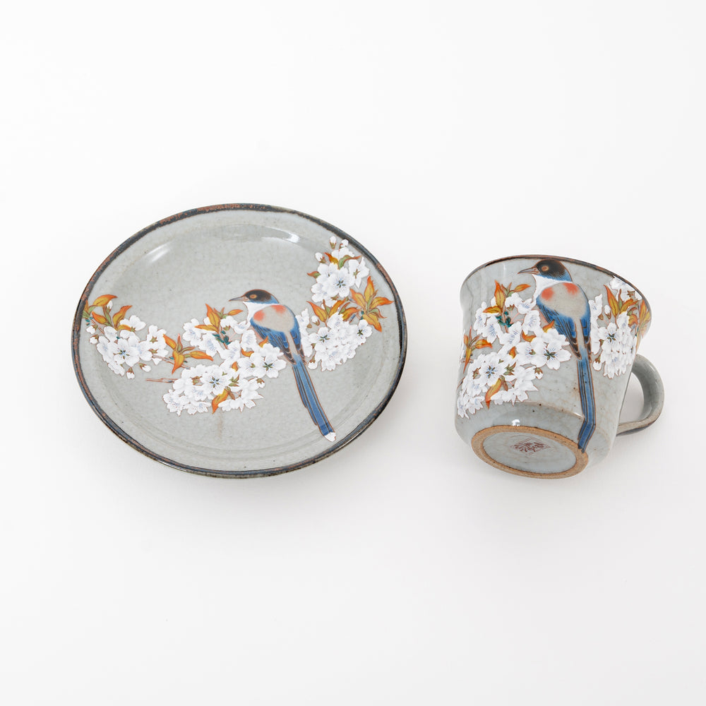 Ceramic cup and saucer set with floral and bird design on a white background