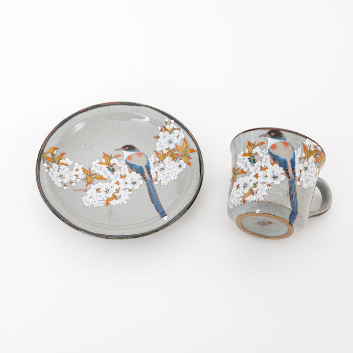 Ceramic cup and saucer set with floral and bird design on a white background