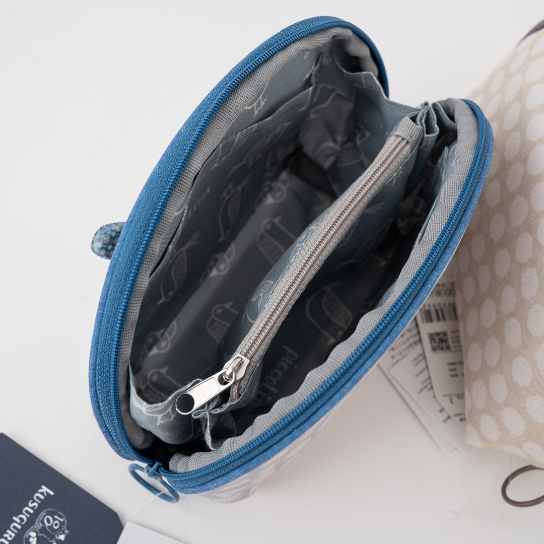 An open blue zippered pouch with a gray patterned interior lining, shown on a white surface next to a partially visible beige polka-dot pouch.
