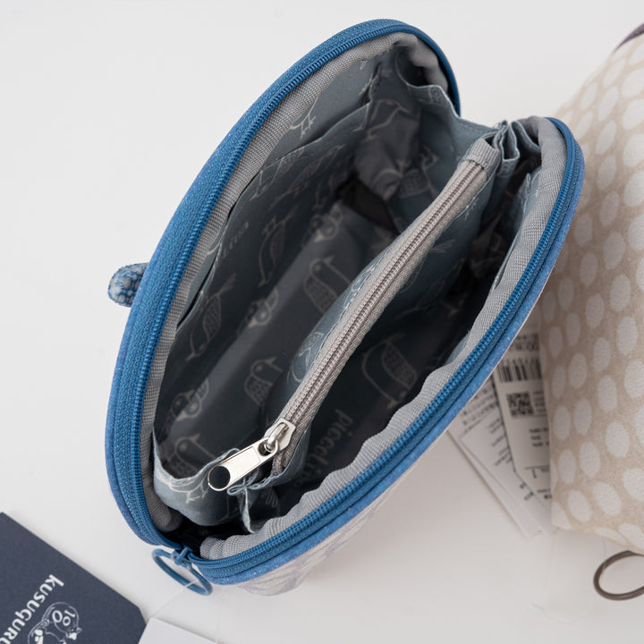 An open blue zippered pouch with a gray patterned interior lining, shown on a white surface next to a partially visible beige polka-dot pouch.