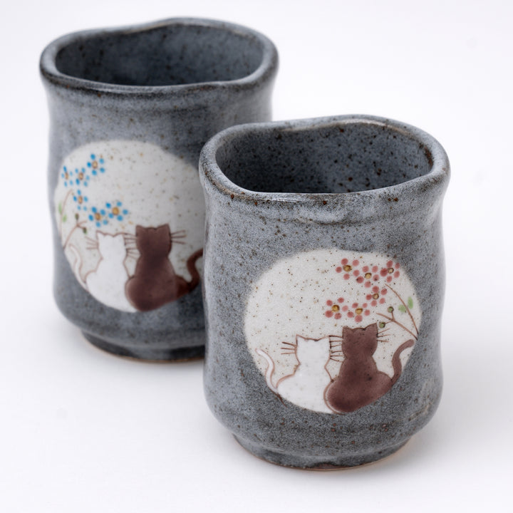 Two ceramic cups with cat and flower designs on a white background