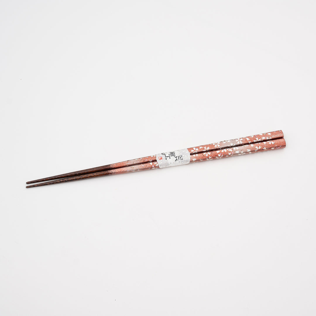 A close-up view of Japanese lacquer chopsticks, showing the white Raden (mother-of-pearl) inlay and delicate floral patterns on a red-brown background.
