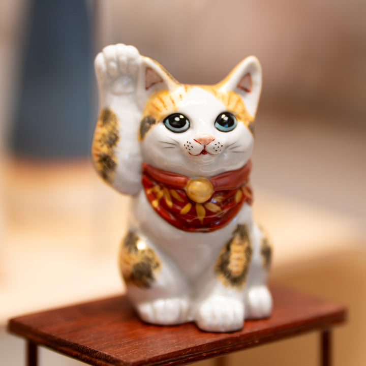 A hand-painted Maneki Neko figurine with a black glaze, featuring a detailed depiction of Mount Fuji, waves, a turtle, and a crane. The figurine has a red neckerchief and gold accents.