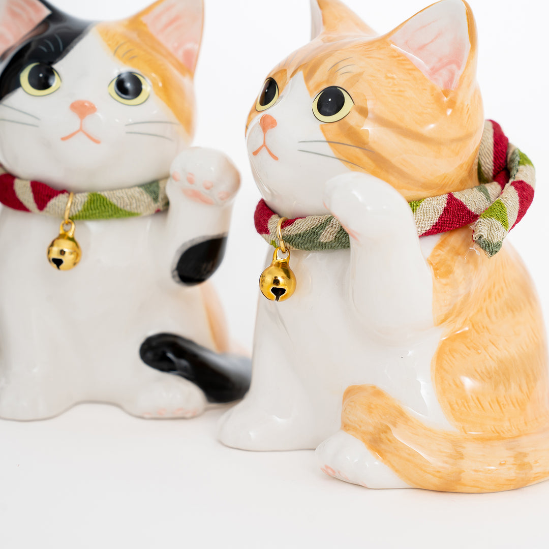 Two ceramic cat figurines with scarves and bell collars on a white background