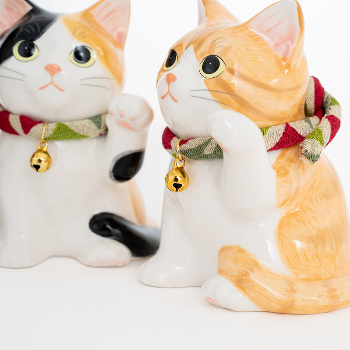 Two ceramic cat figurines with scarves and bell collars on a white background
