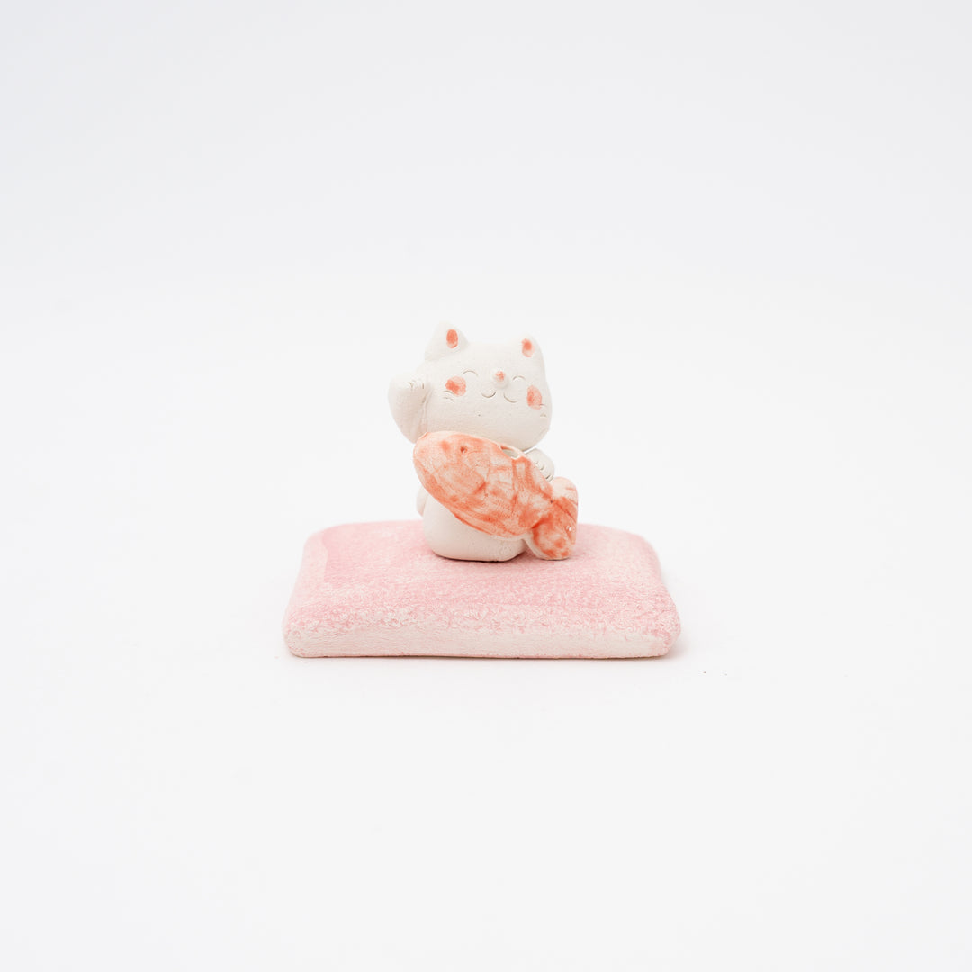 A ceramic incense holder featuring a Maneki Neko (beckoning cat) with a sea bream design, sitting on a pink square plate.