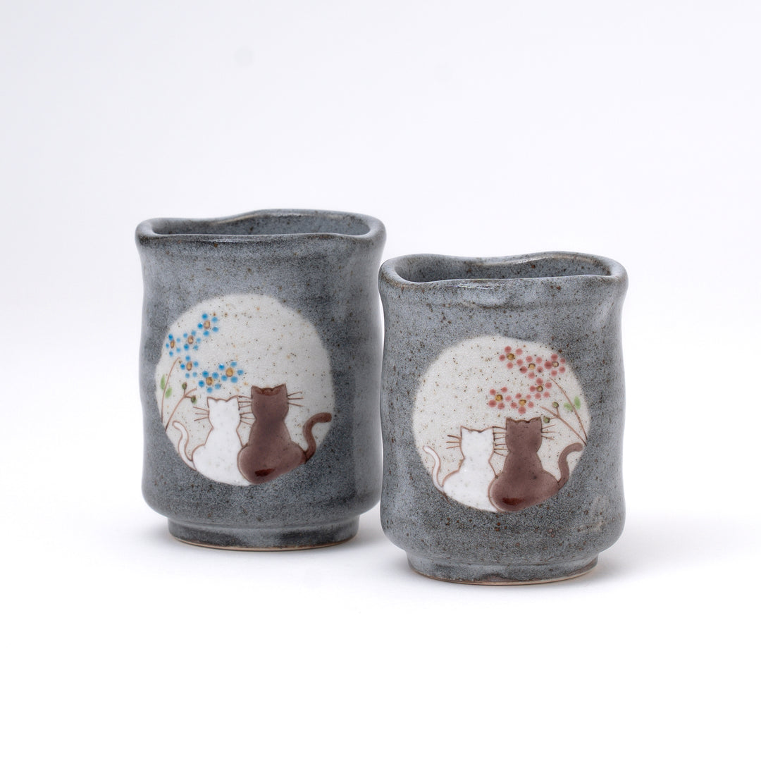 Handmade Kutani ware cat tea cup pair in gray stoneware featuring two cats sitting beneath a full moon with hand-painted blue and pink seasonal blossoms. Made in Japan.