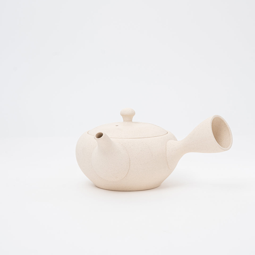 A beige, handmade Tokoname teapot with a spout and lid, isolated on a white background.