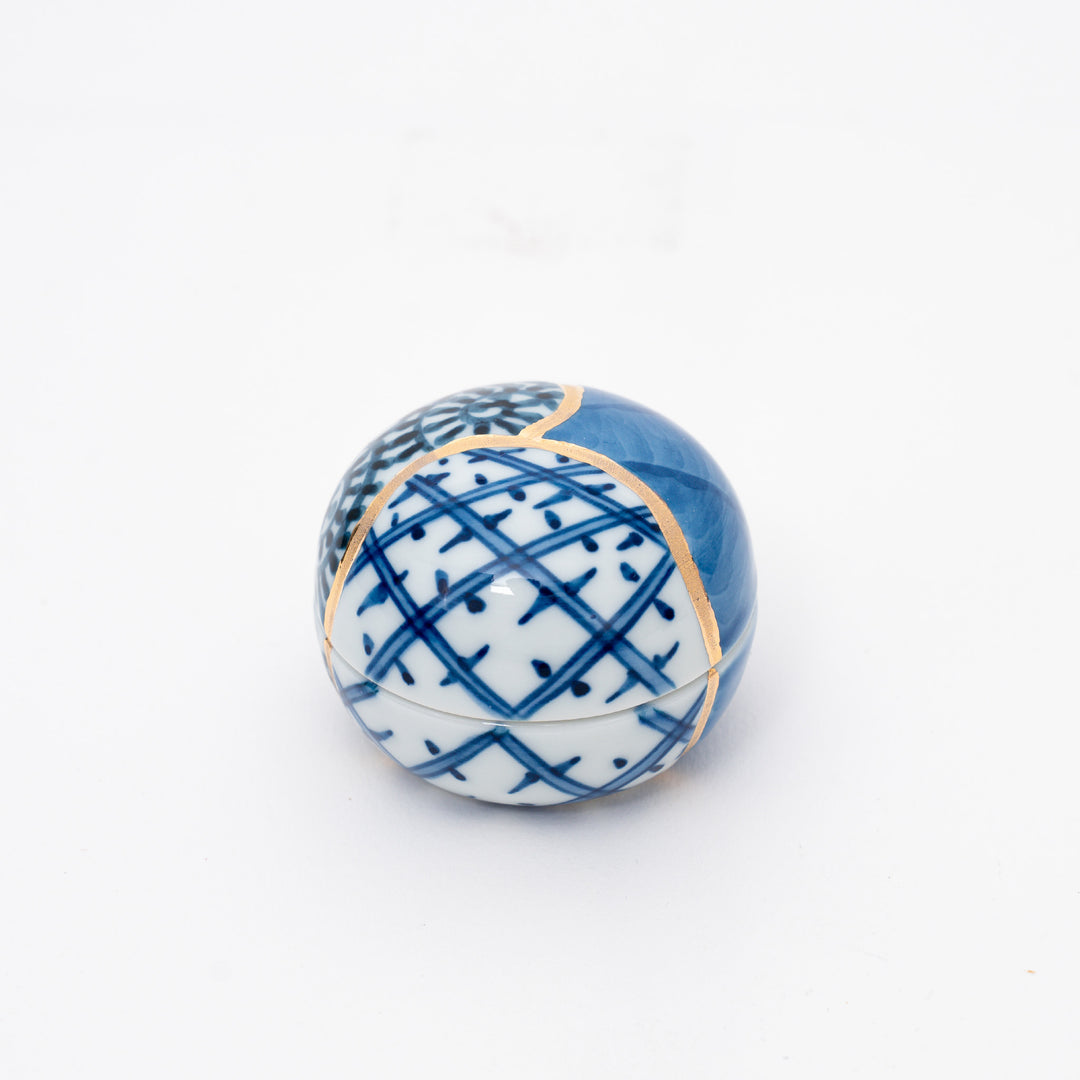 Kintsugi-inspired Arita Ware round porcelain container, blue and white geometric patterns with gold repair accents, used as an omakase sauce dish or decorative ring box.