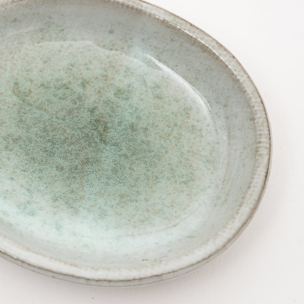 Close-up view of Japanese ceramic dish showing unique speckled gray-green glaze texture and exposed red clay rim