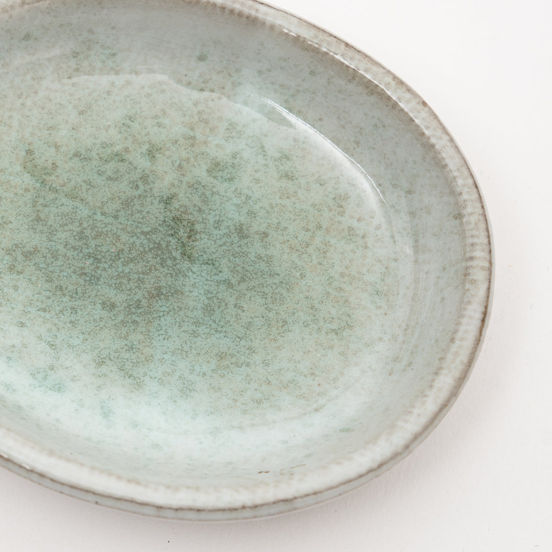 Close-up view of Japanese ceramic dish showing unique speckled gray-green glaze texture and exposed red clay rim