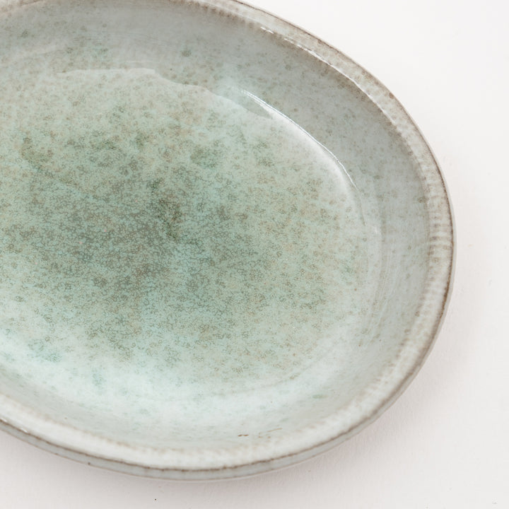 Close-up view of Japanese ceramic dish showing unique speckled gray-green glaze texture and exposed red clay rim