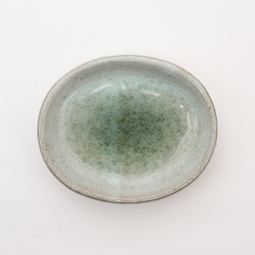Handmade Japanese ceramic dish with speckled gray-green glaze on red clay, featuring irregular oval shape embodying wabi-sabi aesthetic