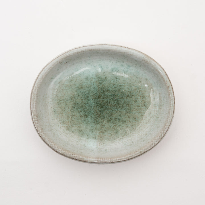 Handmade Japanese ceramic dish with speckled gray-green glaze on red clay, featuring irregular oval shape embodying wabi-sabi aesthetic